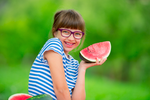 Child eating watermelon. Kids eat fruits in the garden. Pre teen girl in the garden holding a slice of water melon. happy girl kid eating watermelon. Girl kid with gasses and teeth braces