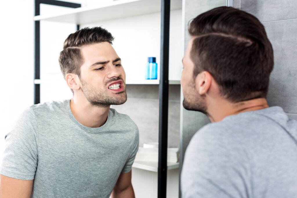 Man looking at teeth in mirror.