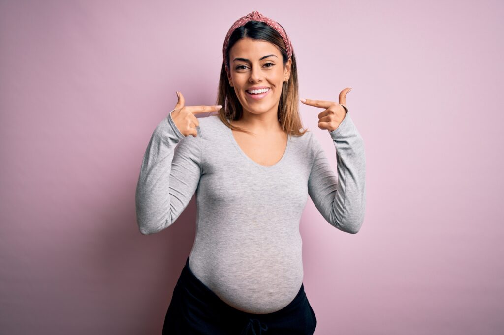 Young pregnant woman happily pointing to straight teeth