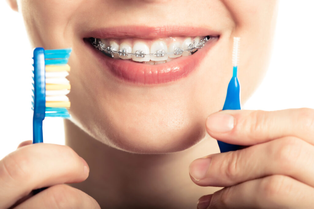 Close up of person with braces, toothbrush, and interdental brush. 