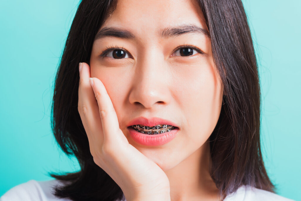 Young woman holding mouth with braces pain from sensitivity. 