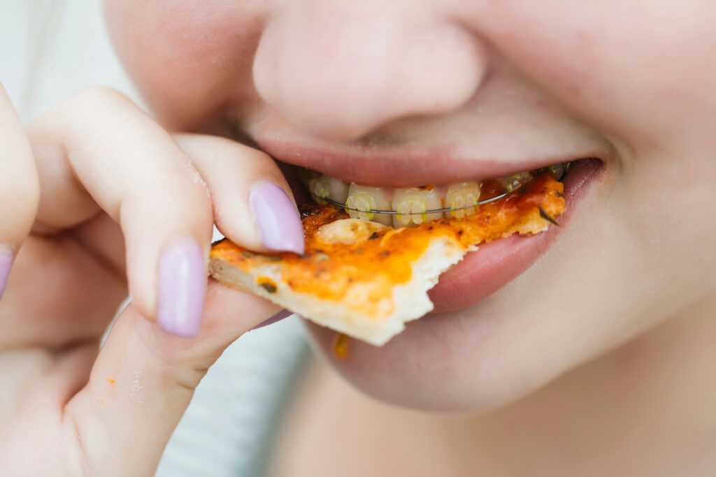 Person with braces biting into pizza.