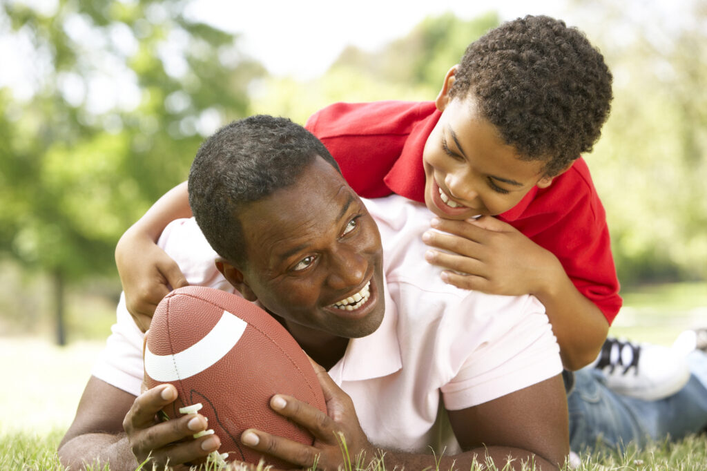 Man smiling playing foot ball with son. 