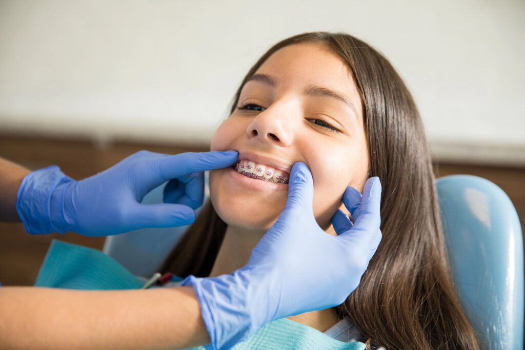 Teen girl having teeth with braces checked by orthodontist.